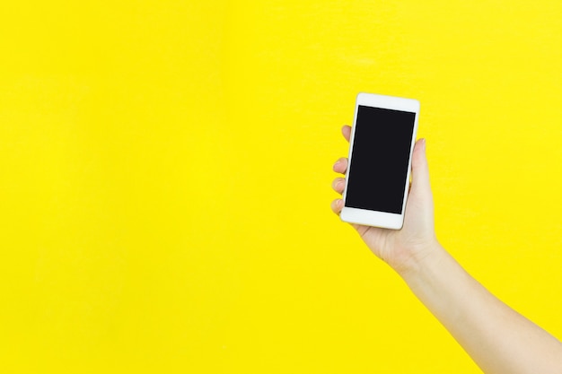 Smartphone in hand on yellow background with copy space for your text.