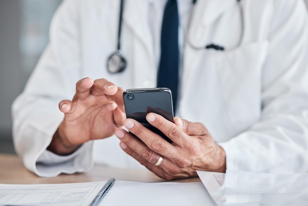 Smartphone hands and doctor typing at table in hospital for research telehealth or healthcare Phone medical professional or surgeon expert or person on wellness app email or online consultation