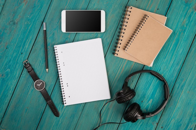 Smartphone headphones watch and notepads on the wooden desk