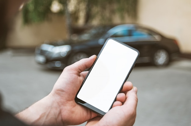 Smartphone in de hand van de man, op de achtergrond een zwarte auto.