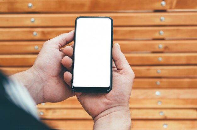 smartphone in de handen van een man, tegen de achtergrond van een houten bank.