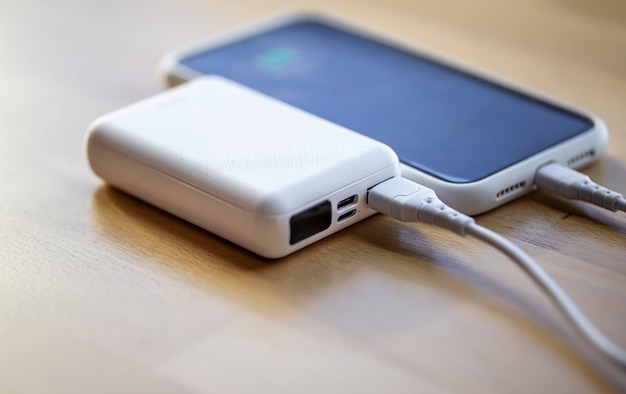 Photo the smartphone is charged from a small white power bank via a cord, close up.