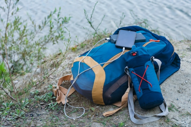 Lo smartphone viene caricato utilizzando un caricabatterie portatile. power bank ricarica il telefono all'aperto con uno zaino per il turismo nella natura.