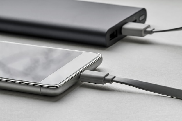 The smartphone is charging from external powerbank with cable