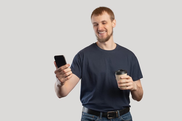 Smartphone in male hands closeupA European man with a phone and coffee in his hands on a gray isolated background