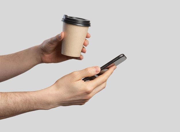 Smartphone in male hands closeupA European man with a phone and coffee in his hands on a gray isolated background