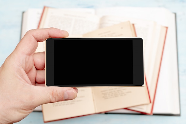 Smartphone in mans hand. Modern gadget phone. Phone screen. Old paper books.