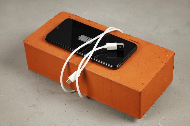 Smartphone met bijna lege batterij ligt op rode baksteen rond oplaadkabel USB is omwikkeld