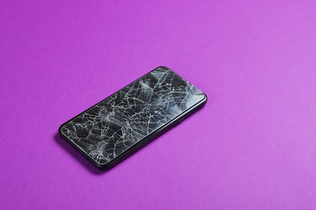 Smartphone met gebroken beschermend glas op paarse tafel.