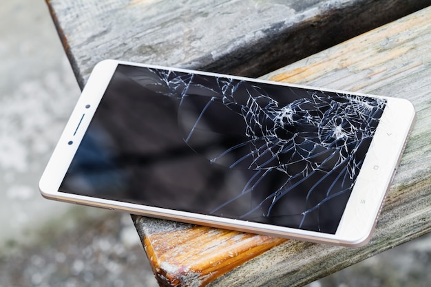 Foto smartphone met gebroken scherm ligt op de houten bank. selectieve aandacht