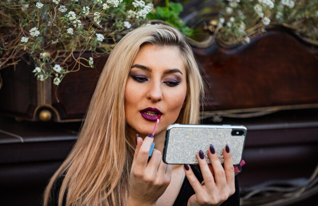 Smartphone mirror. cosmetics review channel. beauty blogger\
concept. apply makeup. girl watching makeup tutorial video.\
lipstick on lips. cosmetics and makeup. get ready for date. always\
looking good.