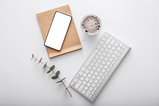 Smartphone mock up met notitie toetsenbord koffiekopje groene plant op witte werkruimte bureau. bovenaanzicht plat lag. mobiele telefoon op moderne bureauwerkruimte.