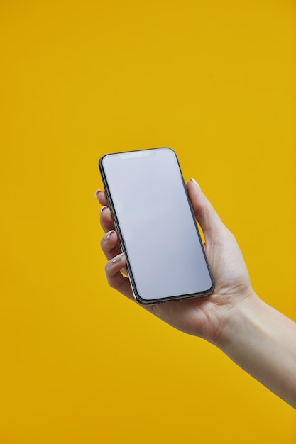 Modello di smartphone. mano femminile che tiene cellulare nero con con esposizione in bianco su fondo giallo