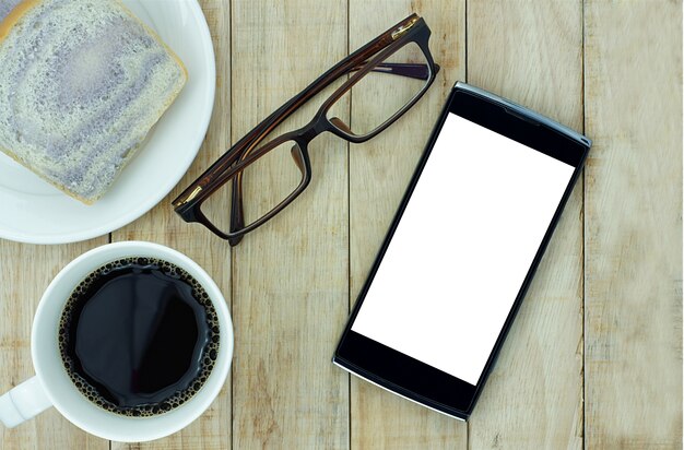 Smartphone, oogglazen en een kopje koffie met brood op houten achtergrond