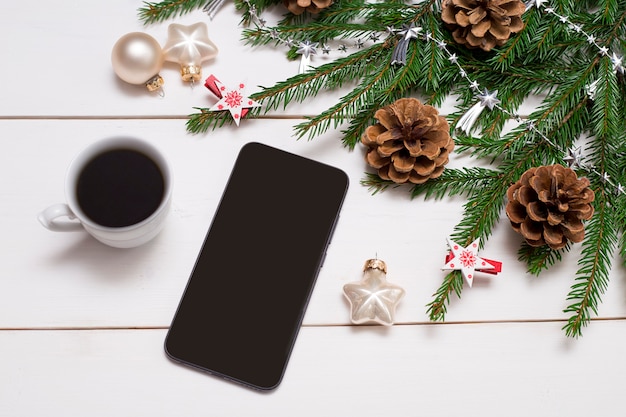 Smartphone op de achtergrond van een kerstboom met speelgoed dennenappels en koffie