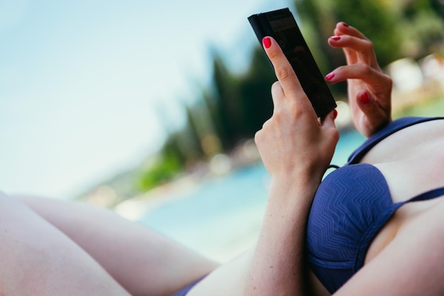 Smartphone op het strand mooi jong meisje met strohoed in bikini ligt op de kiezelstrandvakantie in Italië Knipsel