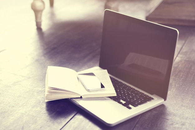 Smartphone on open book and laptop on a floor vintage photo effect