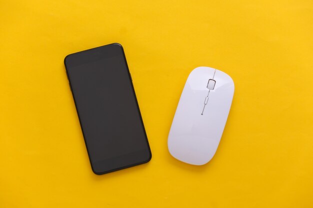 Smartphone and pc mouse on a yellow background. Top view