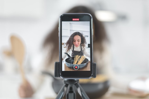 Smartphone che registra il video di una donna latina che prepara la colazione in cucina.