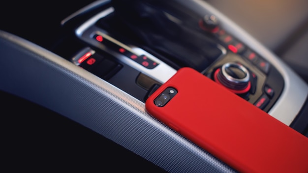 Smartphone in red case on the modern car interior