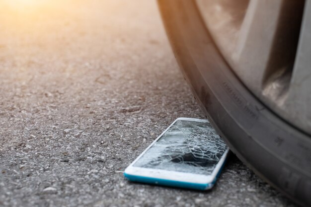 Smartphone screen is cracked flat on the road from moving a car tire at the front