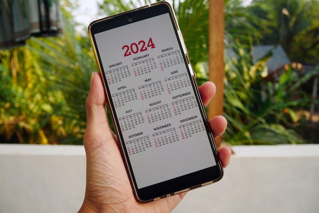 Foto smartphone sullo schermo con calendario per il 2024 in mani maschili telefono android con calendario per el 2024 su s