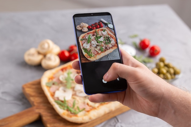 Smartphone girato cibo. pizza tradizionale italiana con formaggio, prosciutto e funghi. reti sociali e concetto di applicazione alimentare di consegna.