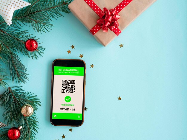 スマートフォンは、クリスマスの背景にcovid19コロナウイルスに対する予防接種の証明書を示しています