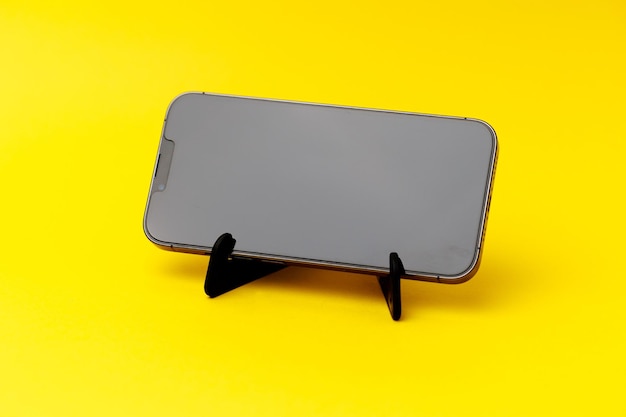 Smartphone standing on a black smartphone stand isolated on the yellow background