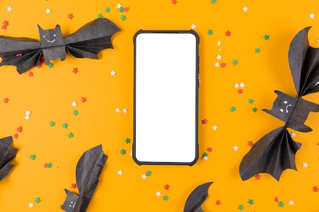 Photo smartphone surrounded by bats made of paper on orange. flat lay
