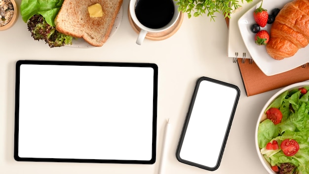 A smartphone and tablet blank screen mockup on white table background surrounded with healthy food