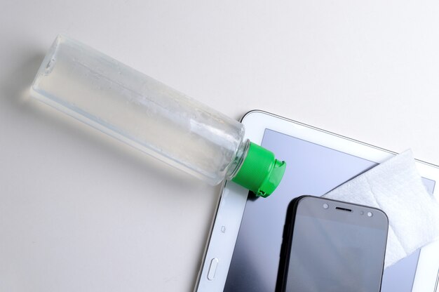 젤 소독제와 냅킨 병 장소에 흰색 배경에 스마트 폰 및 태블릿. 웨어러블 기기의 항 바이러스 및 항균 처리.