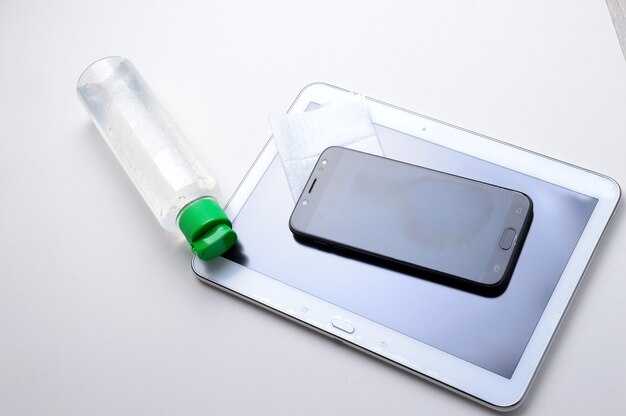 Smartphone and tablet with a bottle of gel sanitizer and napkin. antiviral and antibacterial treatment of wearable gadgets.