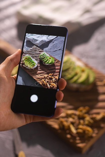 Smartphone che scatta foto da panini biologici sani con avocado man mano