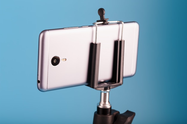 青い背景の写真ビデオカメラとしての三脚のスマートフォン。ブログのビデオと写真を記録します。