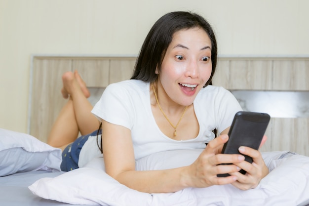 Smartphone van het vrouwen Aziatische wauw gezicht op het bed