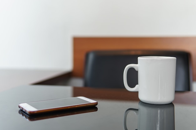 Smartphone and white cup of coffee on a table in cafe.