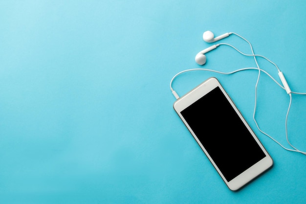 Smartphone. white phone and headphones on a bright light blue background. top view. space for text