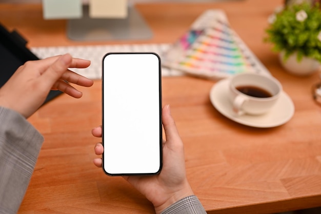 Smartphone white screen mockup in a woman's hand over modern office desk