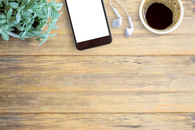 Smartphone white screen white ear phone and cup of coffee on wooden table background