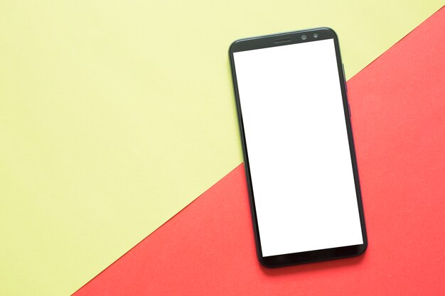 Smartphone with blank screen on colored paper. Top view. 