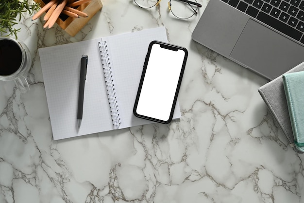 Фото Смартфон с блокнотом для ноутбука с пустым экраном и очками на мраморном столе плоский вид сверху