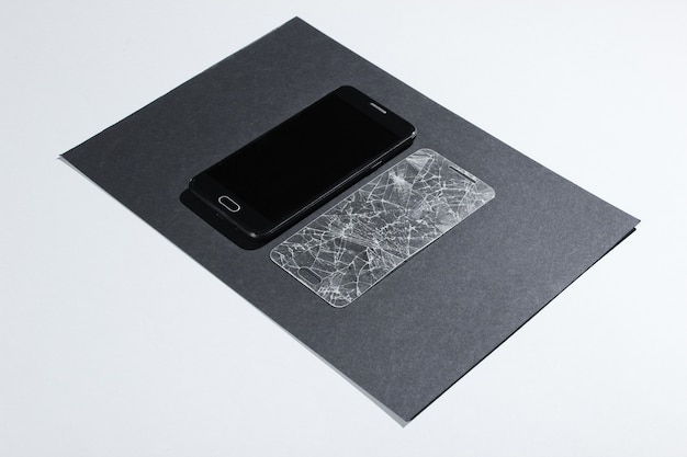 紙のテーブルに壊れた保護ガラス付きのスマートフォン。側面図