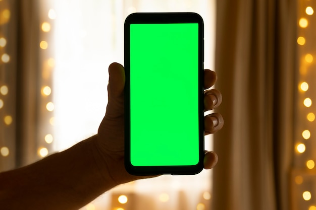 Smartphone with Green Mockup Screen Green Chroma Key Screen Phone is in a Hand in the Living Room