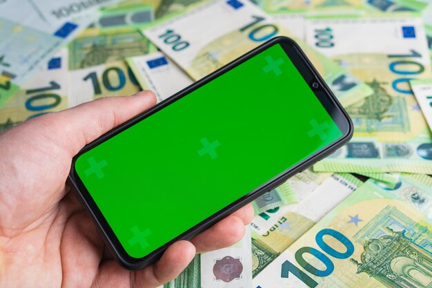 Smartphone with green screen for advertising app in hand at euro banknotes background Mock up