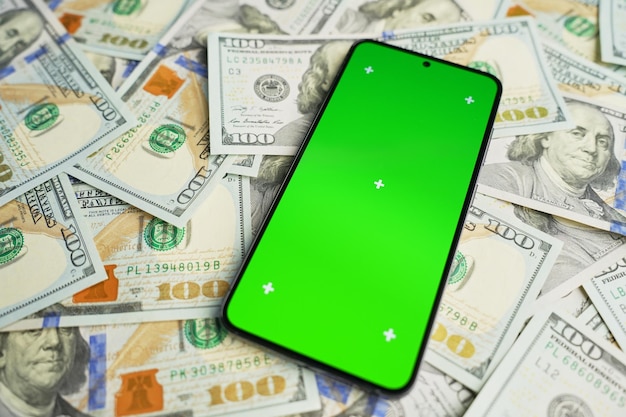 달러 지폐 어리에 초록색 화면을 가진 스마트폰 상단 뷰