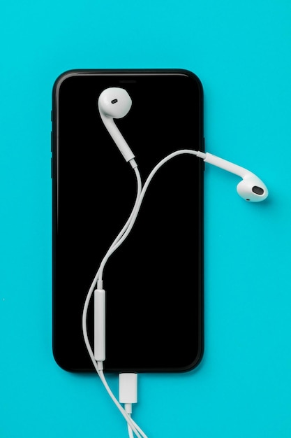 Foto smartphone con cuffie su sfondo blu la vista dall'alto ascolta la musica