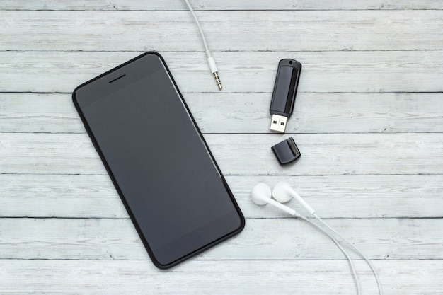 Photo smartphone with headphones and a flash drive on a wooden background, music storage concept