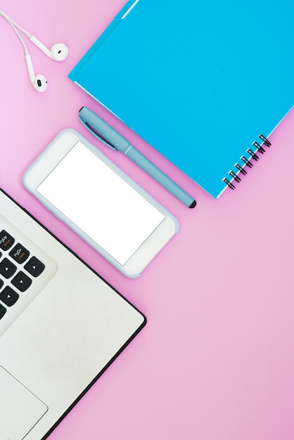 Smartphone with headphones, notebook and notepad on pink background. Top view. Working space Flat Lay Layout