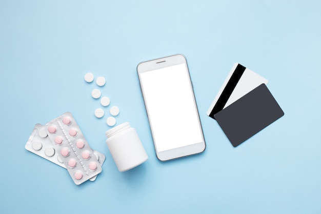 Photo smartphone with pills and credit card on a blue background. stay home concept. pharmacy online shopping. flat lay, top view.